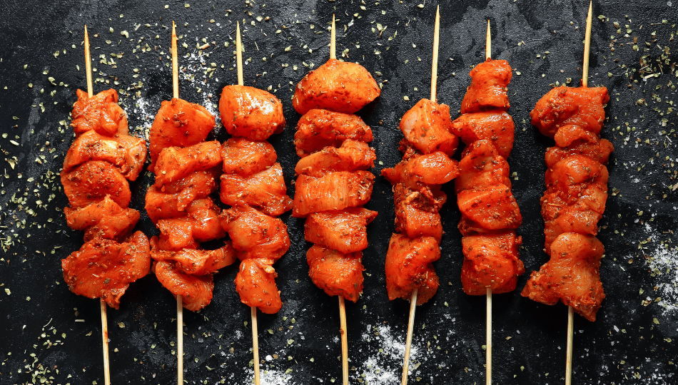 Marinierte Hähnchenspieße auf Holzspießen nebeneinander auf dunklem Untergrund aufgereiht – bereit zum Hähnchen asiatisch Marinieren und Grillen.